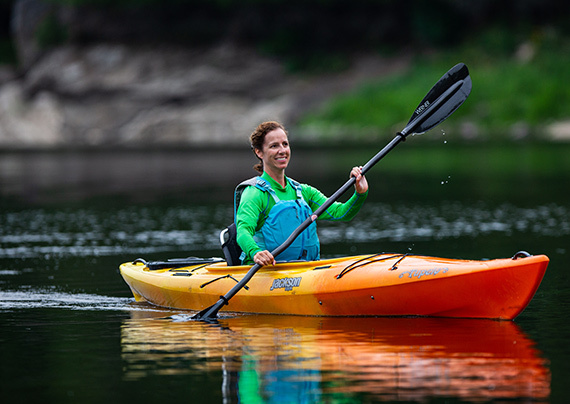 Happy woman paddling a Tupelo Jackson Kayak on a peaceful lake